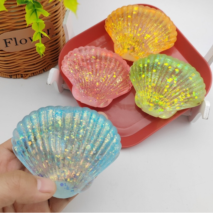 Colorful shell-shaped squishies on a tray with a hand holding a blue shell squishie.