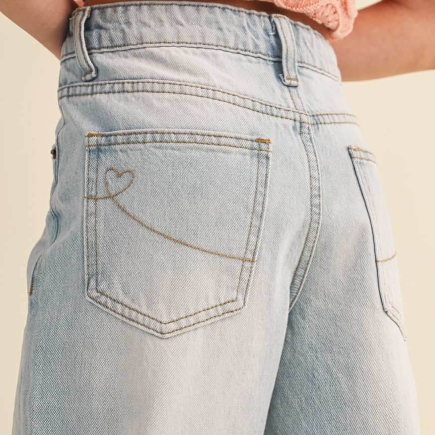 Light blue jeans with a heart design on the pocket against a beige background