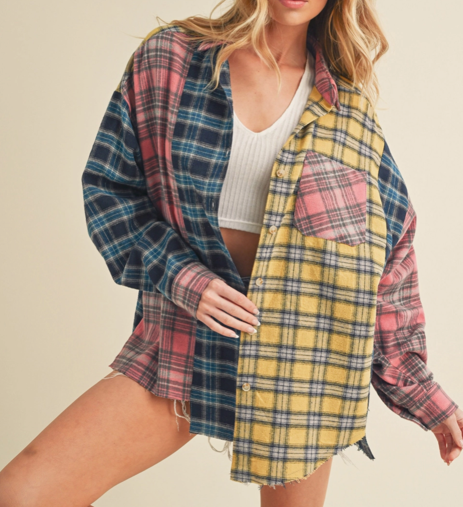 A woman modeling a long-sleeve, oversized plaid button-up shirt with a color-blocked design featuring yellow, pink, and blue plaid panels, worn open over a white ribbed crop top.