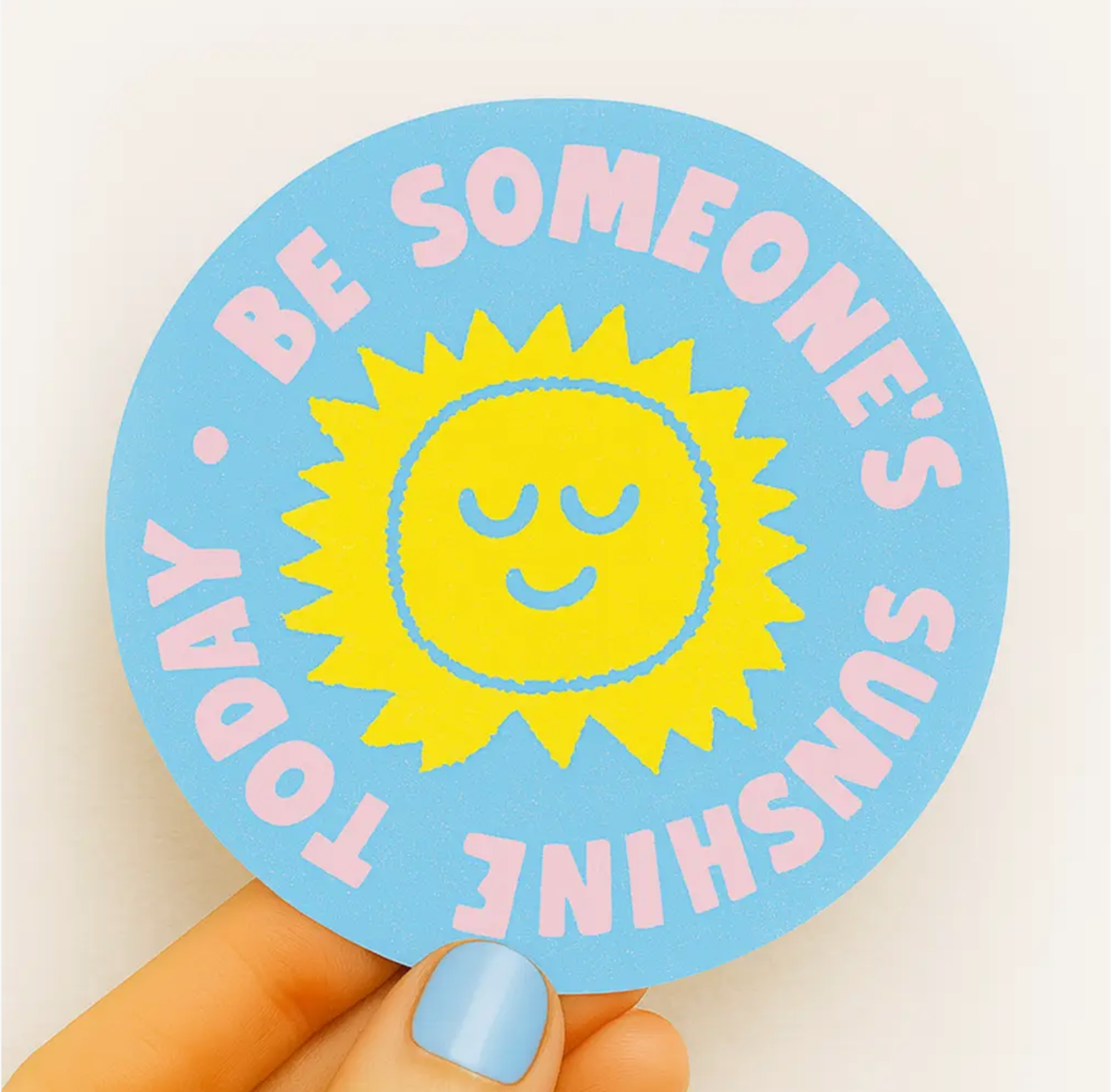 Circular sticker with a sun illustration and text held by a hand on a light background